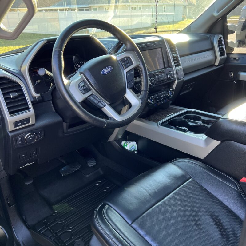 A close-up view of a polished car hood reflecting surrounding trees, showcasing the shine and detailing work.