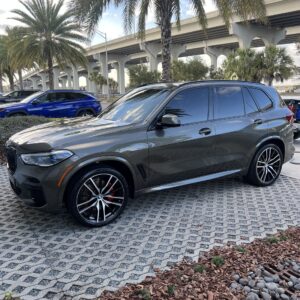A detailed view of a shiny car's exterior, showcasing the reflection of trees and a clear sky, emphasizing the quality of the
